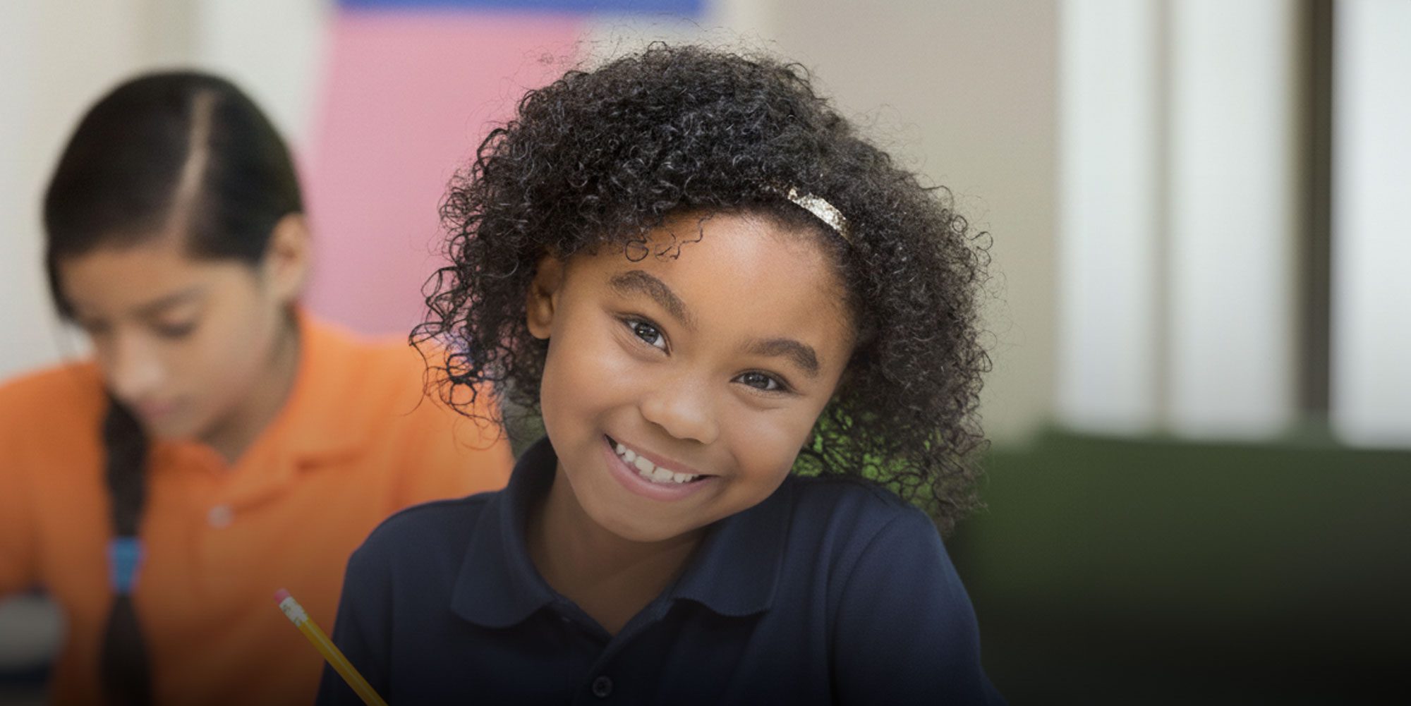 Smiling student holding a pencil at a desk.
