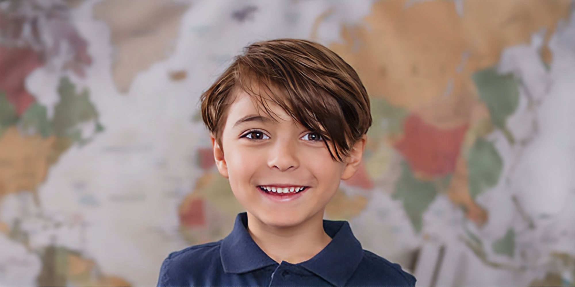 Smiling student in a school uniform in front of a world map.